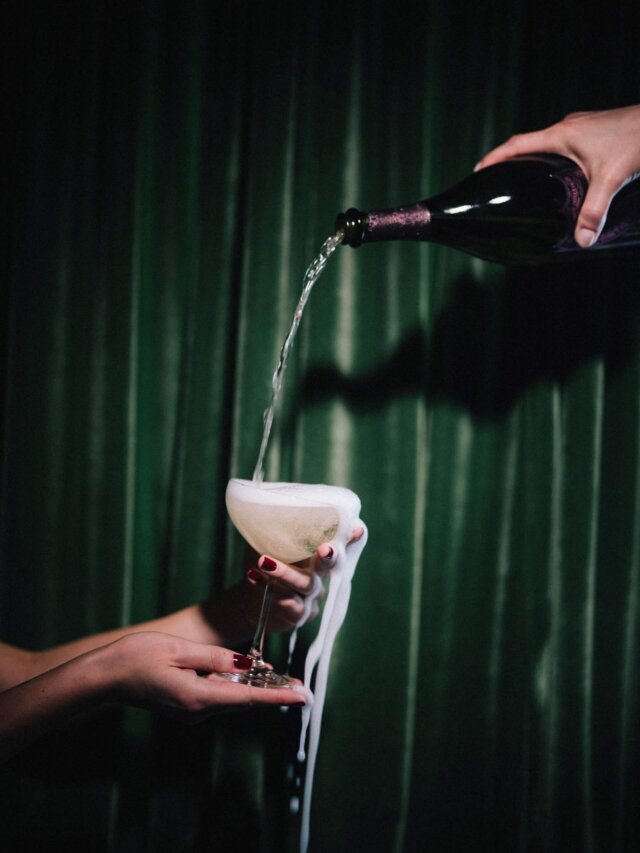 Champagner wird kunstvoll in ein Glas gegossen, während Schaum über den Rand fließt, vor einem eleganten grünen Hintergrund.