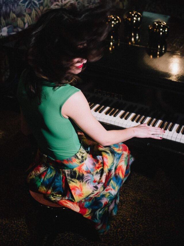 Frau mit buntem Rock spielt lebhaft Klavier im Hotel Edelweiss, Lech/Zürs am Arlberg. Elegante Atmosphäre und Stil.