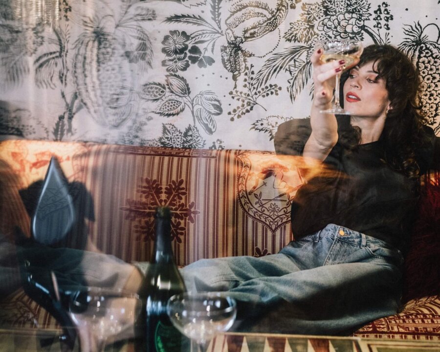 Eine Frau genießt einen Cocktail in der stilvollen Lounge des Hotel Edelweiss in Lech/Zürs, umgeben von elegantem Design.