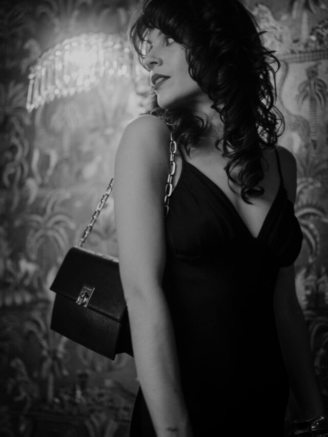 Elegante Frau in schwarzem Kleid mit Handtasche in stylischer Hotelumgebung in Lech/Zürs am Arlberg.
