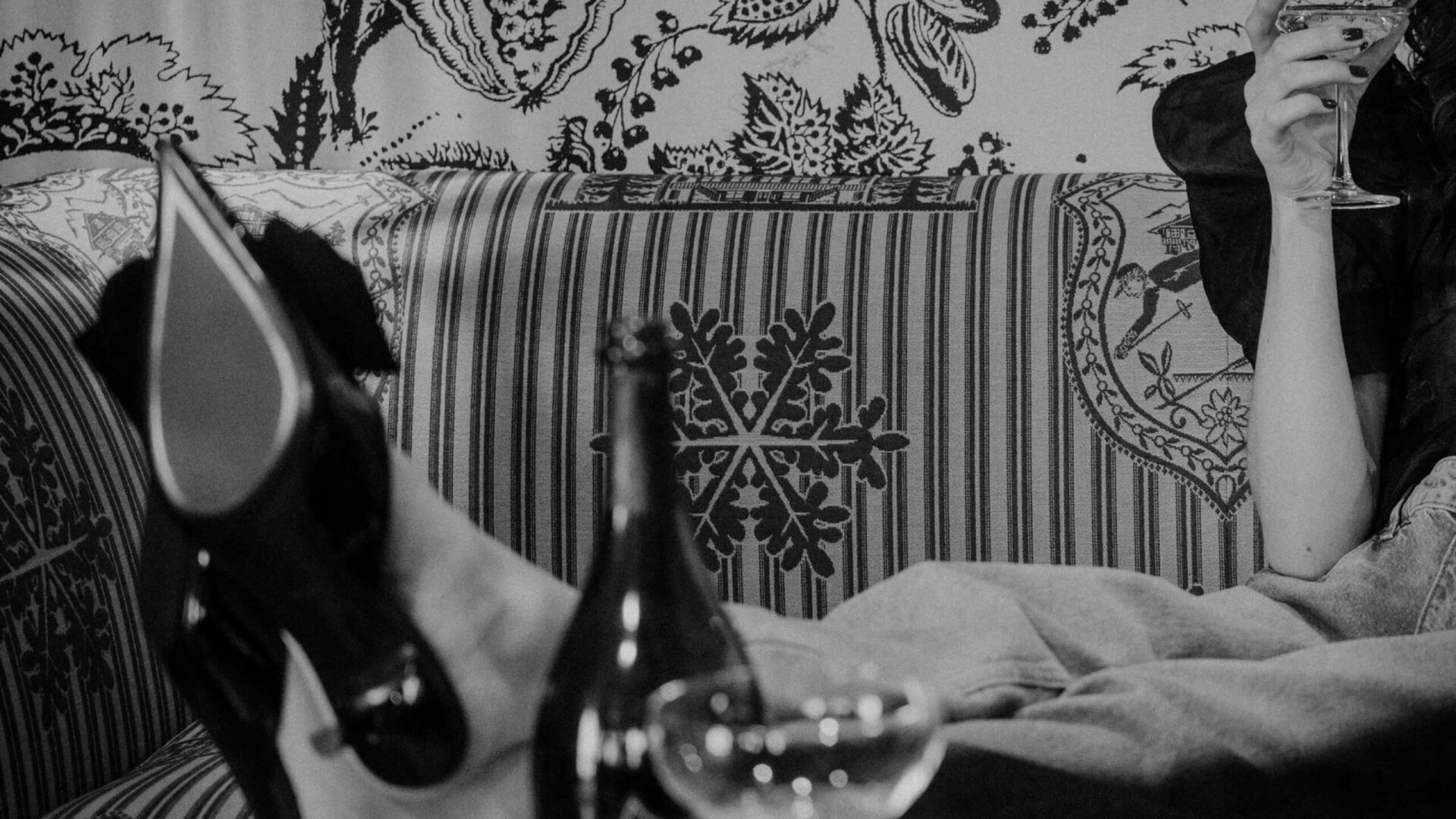 Elegante Füße in schwarzen Schuhen auf einem Sofa, während ein Drink serviert wird. Stilvolles Ambiente im Hotel Edelweiss.