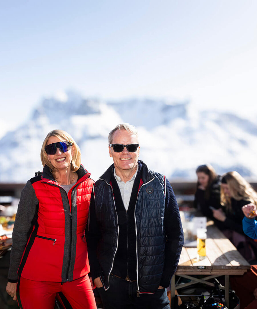 Paar in moderner Skibekleidung genießt die alpine Aussicht auf der Terrasse des Hotels Edelweiss in Lech.