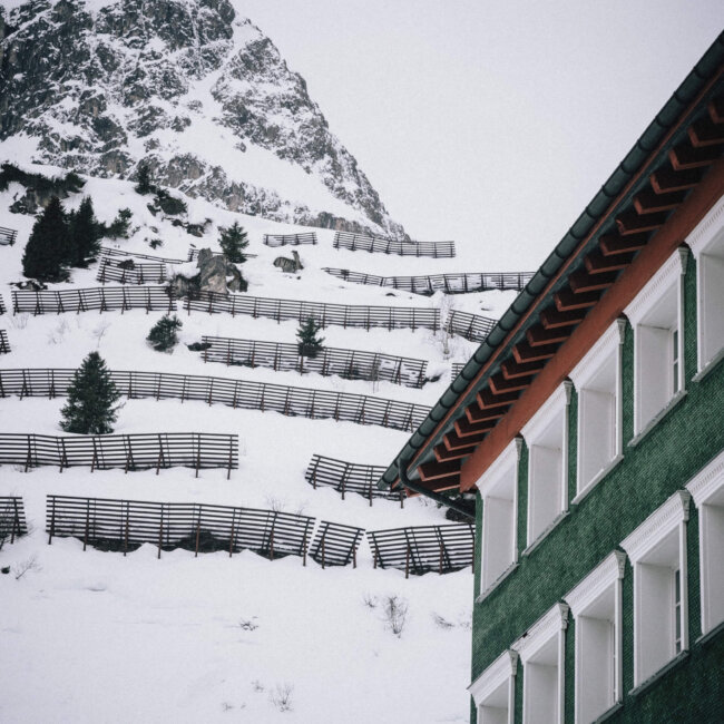 Hotel Edelweiss in Lech mit schneebedecktem Berg und typischen Zaunstrukturen im Winter.