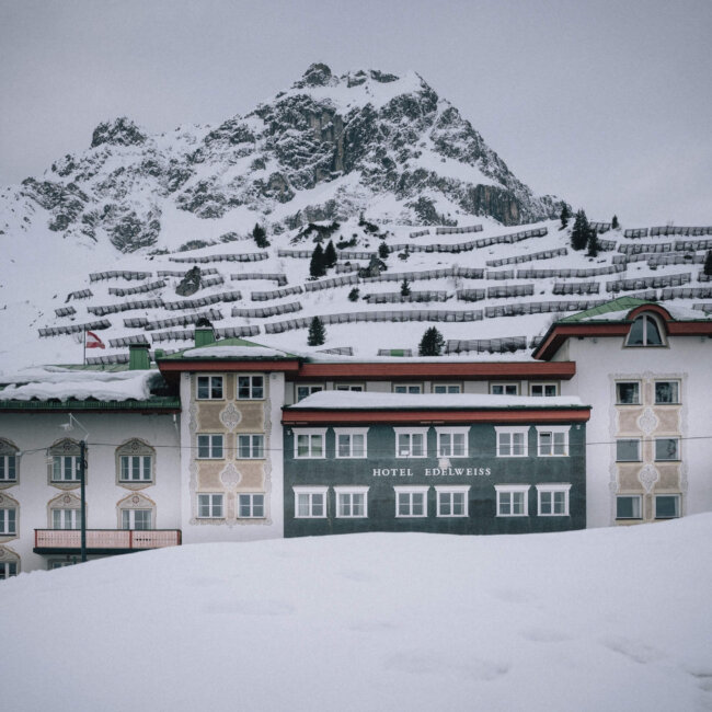 Hotel Edelweiss in Lech/Zürs, umgeben von verschneiten Bergen und winterlicher Landschaft. Idealer Ort für Wintersport.