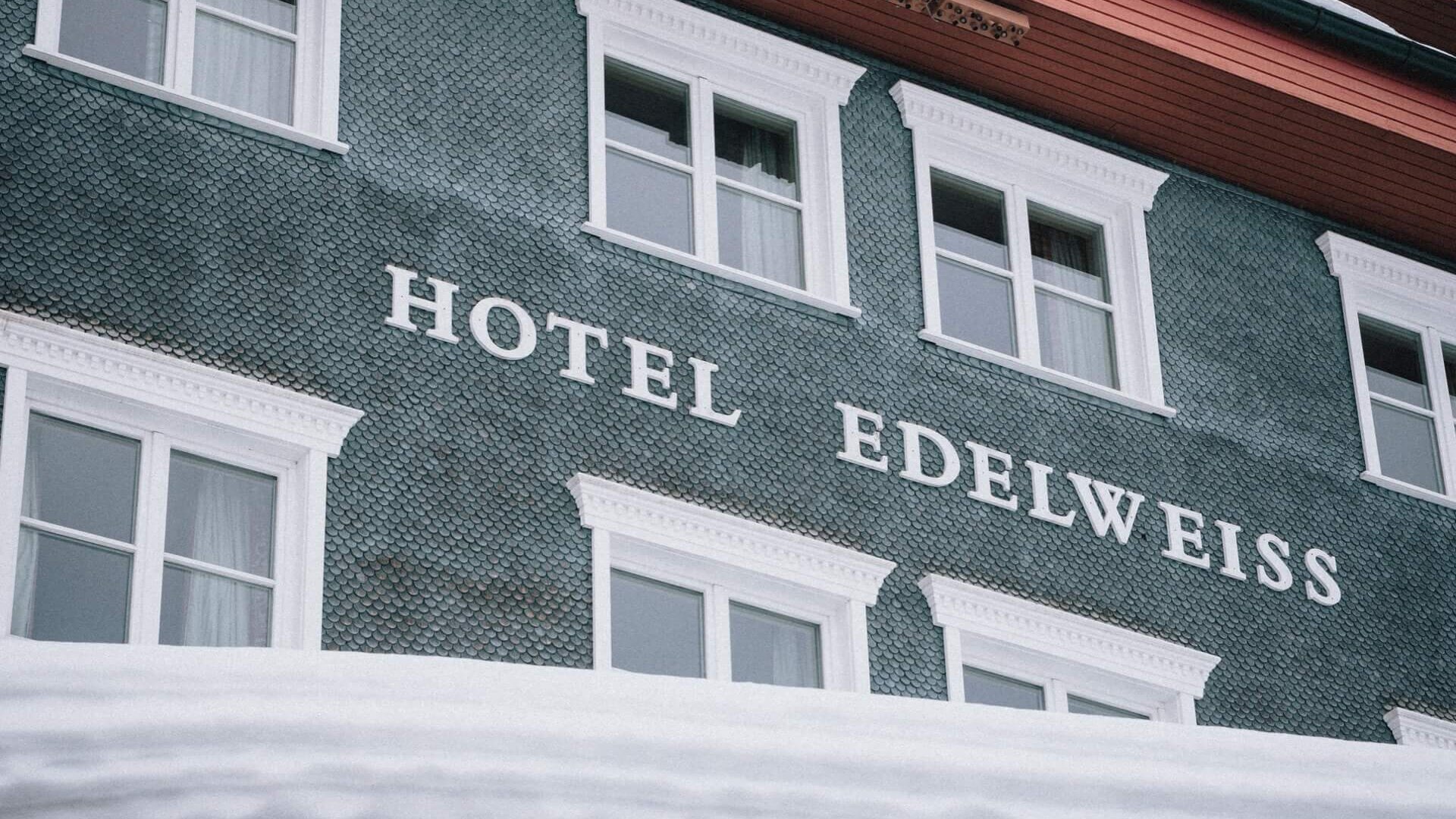 Das Hotel Edelweiss in Lech/Zürs, elegante Architektur mit schneebedecktem Dach und einladenden Fenstern.