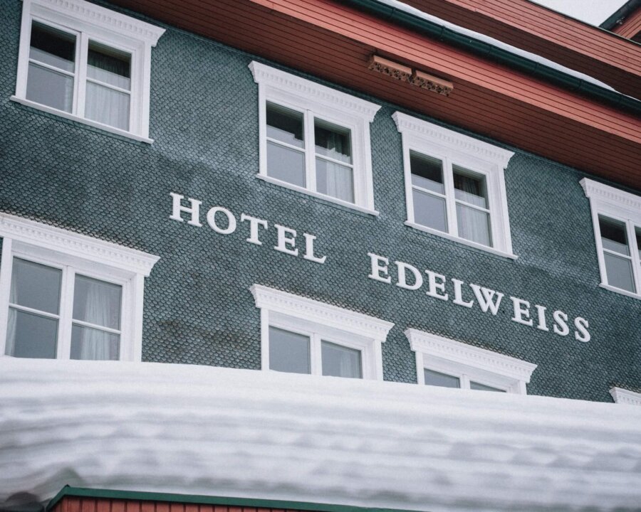 Das Hotel Edelweiss in Lech/Zürs, elegante Architektur mit schneebedecktem Dach und einladenden Fenstern.