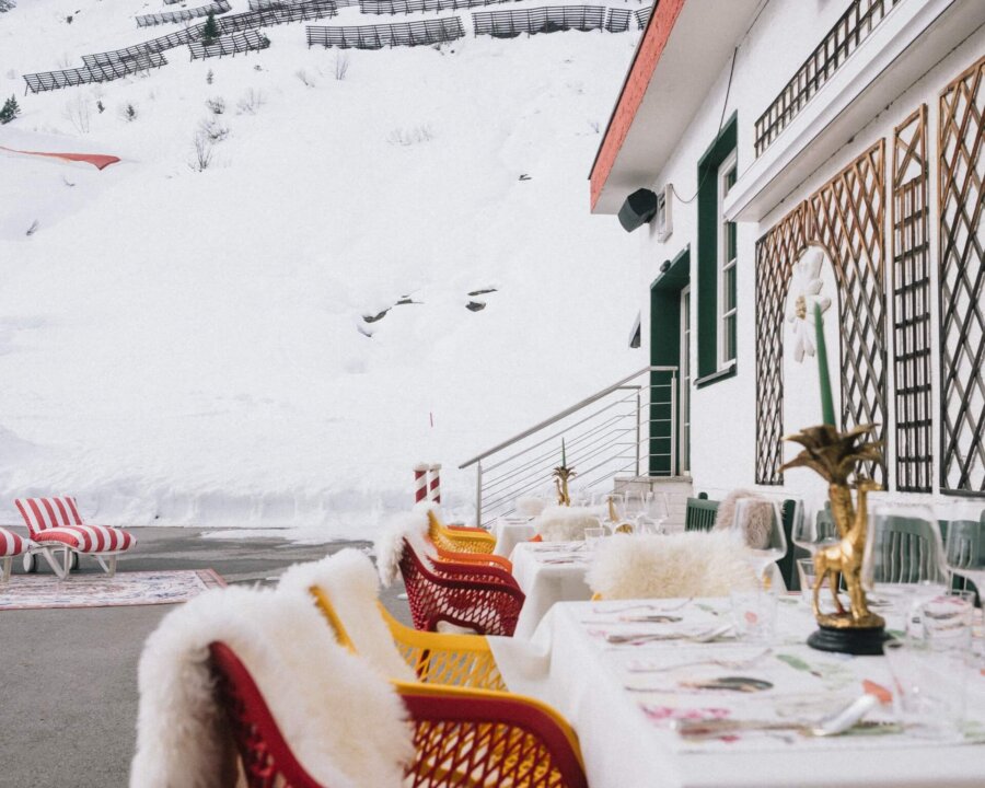Gemütlicher Außenbereich des Hotels Edelweiss in Lech/Zürs, umgeben von schneebedeckten Bergen und stilvollen Möbeln.