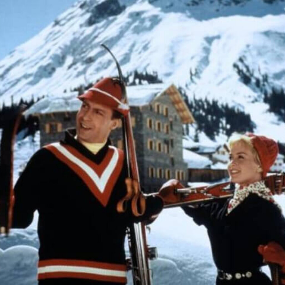 Skifahrer-Paar lächelt glückselig vor einer winterlichen Berglandschaft in Lech am Arlberg. Ideale Kulisse für den Winterurlaub.