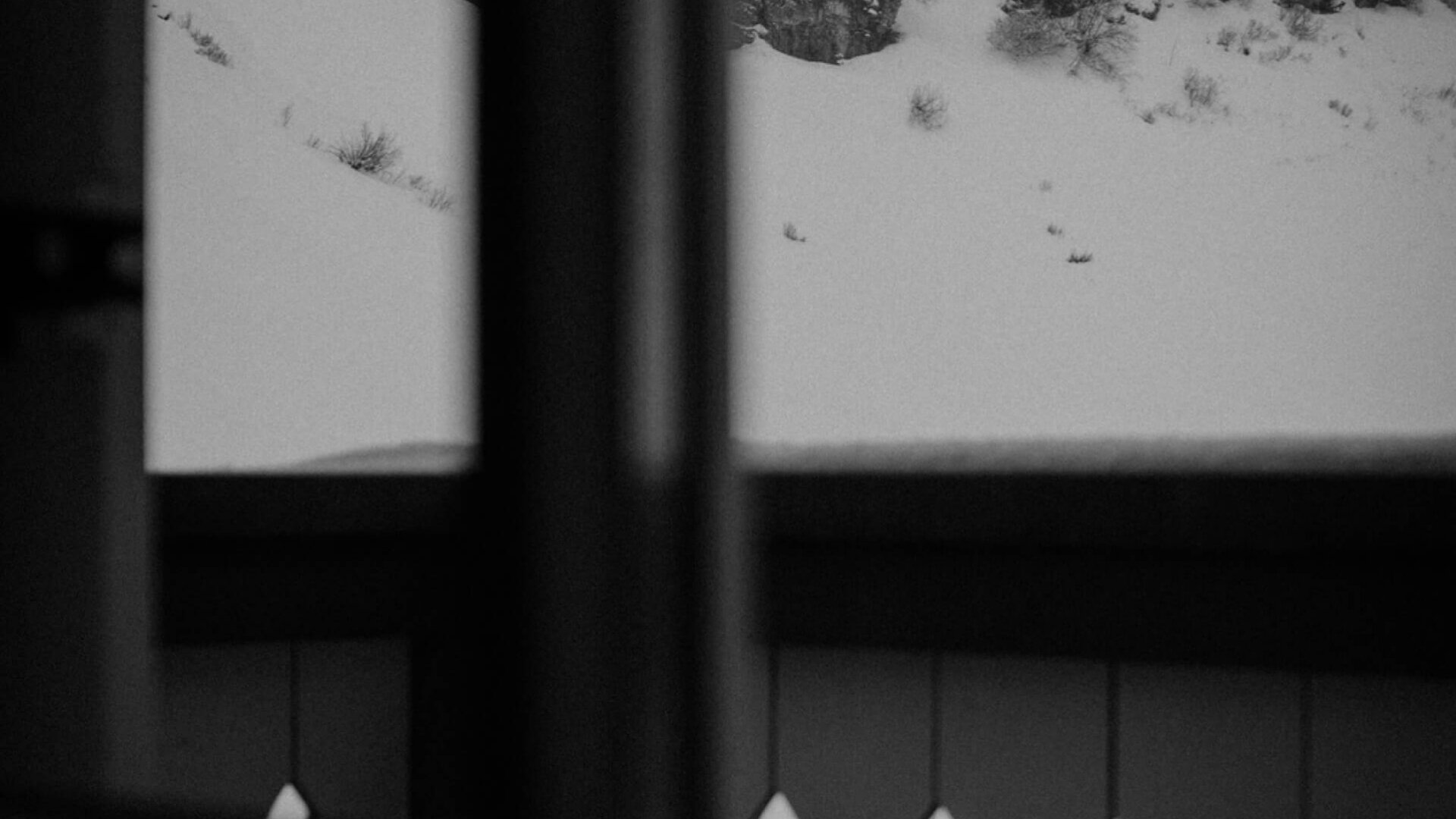 Blick auf schneebedeckte Hügel und Skilifte vom Hotel Edelweiss in Lech/Zürs, durch ein Fensterrahmen in Schwarzweiß.
