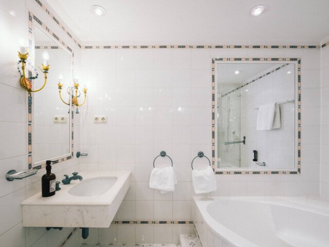 Elegantes Badezimmer im Hotel Edelweiss mit klassischer Badewanne, Waschbecken und stilvollen Wandlampen.
