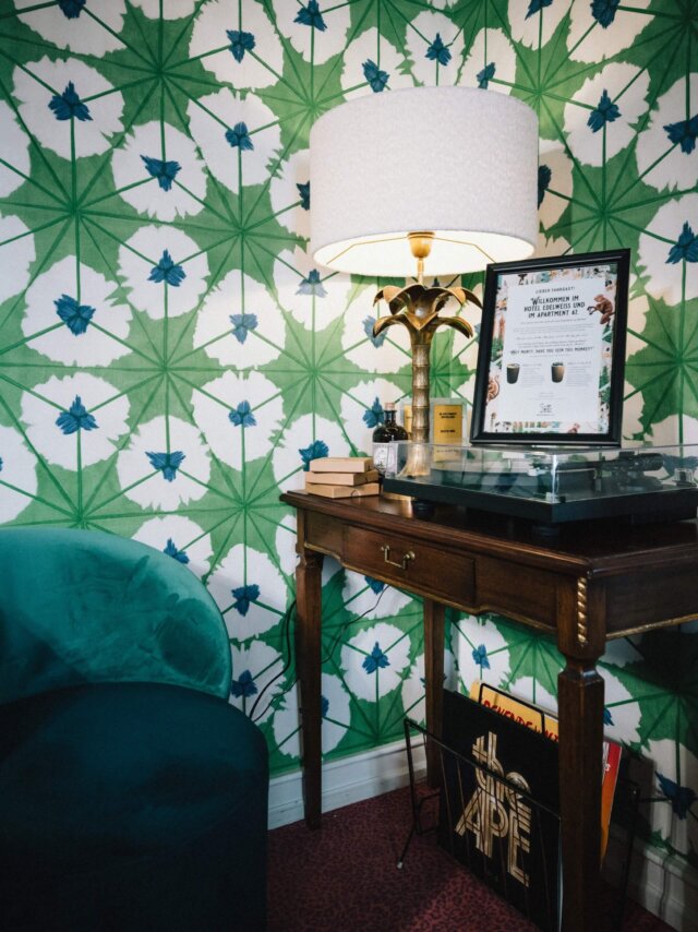 Gemütliche Ecke im Hotel Edelweiss mit elegantem Tisch, Lampe und buntem Wanddesign im Hintergrund.