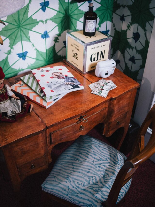 Holzschreibtisch mit Zeitschriften, Fotokamera und einem Gin-Behälter im Hotel Edelweiss in Lech/Zürs. Stilvolles Ambiente.