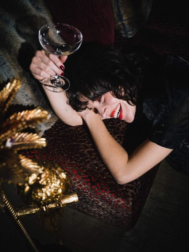 Freudestrahlende Frau mit Cocktailglas auf einem eleganten Sofa im Hotel Edelweiss in Lech/Zürs am Arlberg.