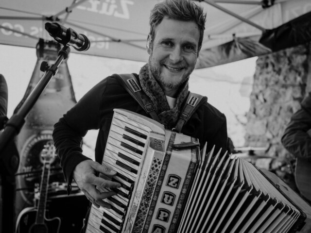 Mann spielt mit Freude auf einem Akkordeon bei einer musikalischen Darbietung im Freien, umgeben von festlicher Stimmung.