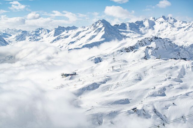 Panoramablick auf verschneite Berge und Skilifte in Lech/Zürs am Arlberg bei strahlend blauem Himmel.