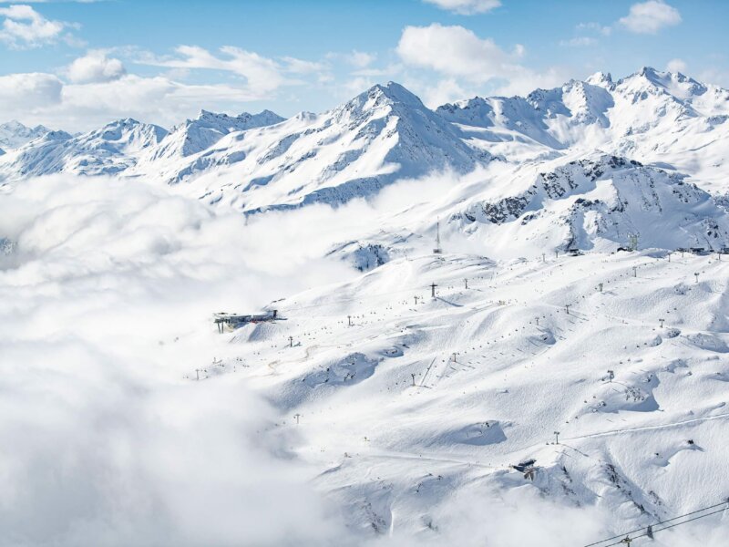 Panoramablick auf verschneite Berge und Skilifte in Lech/Zürs am Arlberg bei strahlend blauem Himmel.