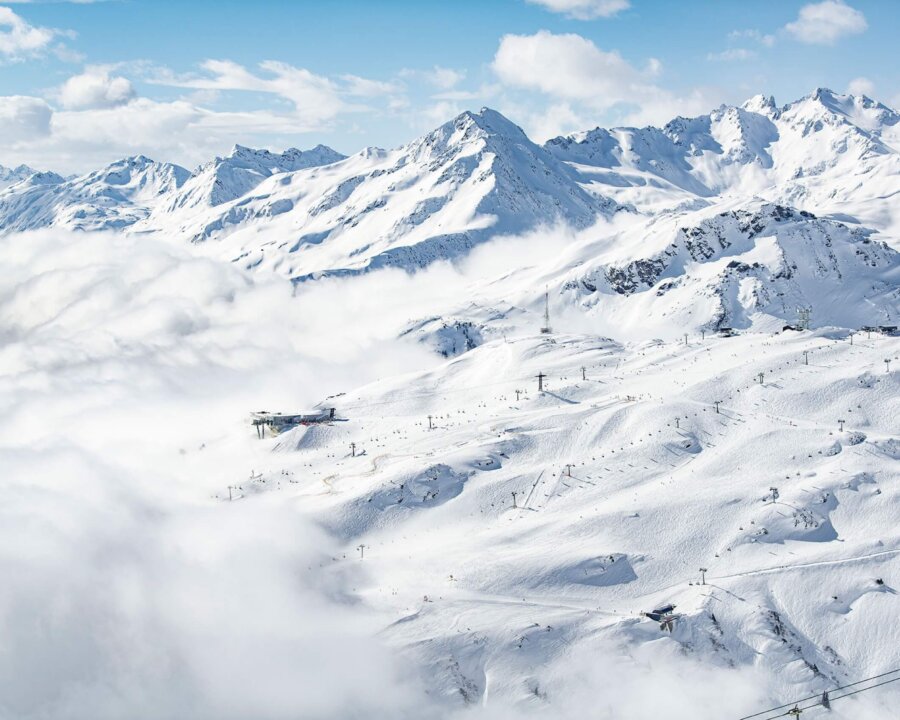 Panoramablick auf verschneite Berge und Skilifte in Lech/Zürs am Arlberg bei strahlend blauem Himmel.