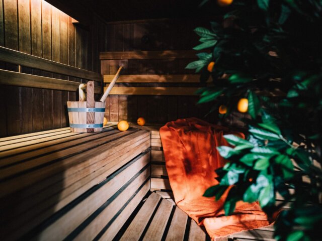 Gemütliche Sauna im Hotel Edelweiss mit Holzbank, Aufgusszubehör und einem orangefarbenen Handtuch zur Entspannung.