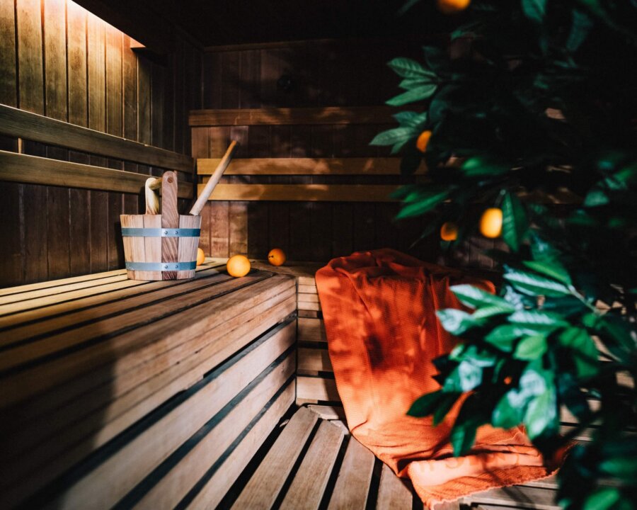 Gemütliche Sauna im Hotel Edelweiss mit Holzbank, Aufgusszubehör und einem orangefarbenen Handtuch zur Entspannung.