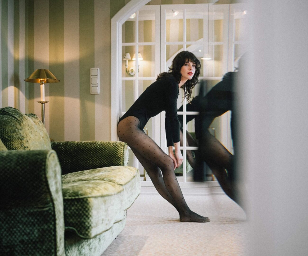 Elegante Frau in einem stilvollen Hotelzimmer im Hotel Edelweiss, Lech/Zürs, mit einem grünen Sofa und Spiegel.