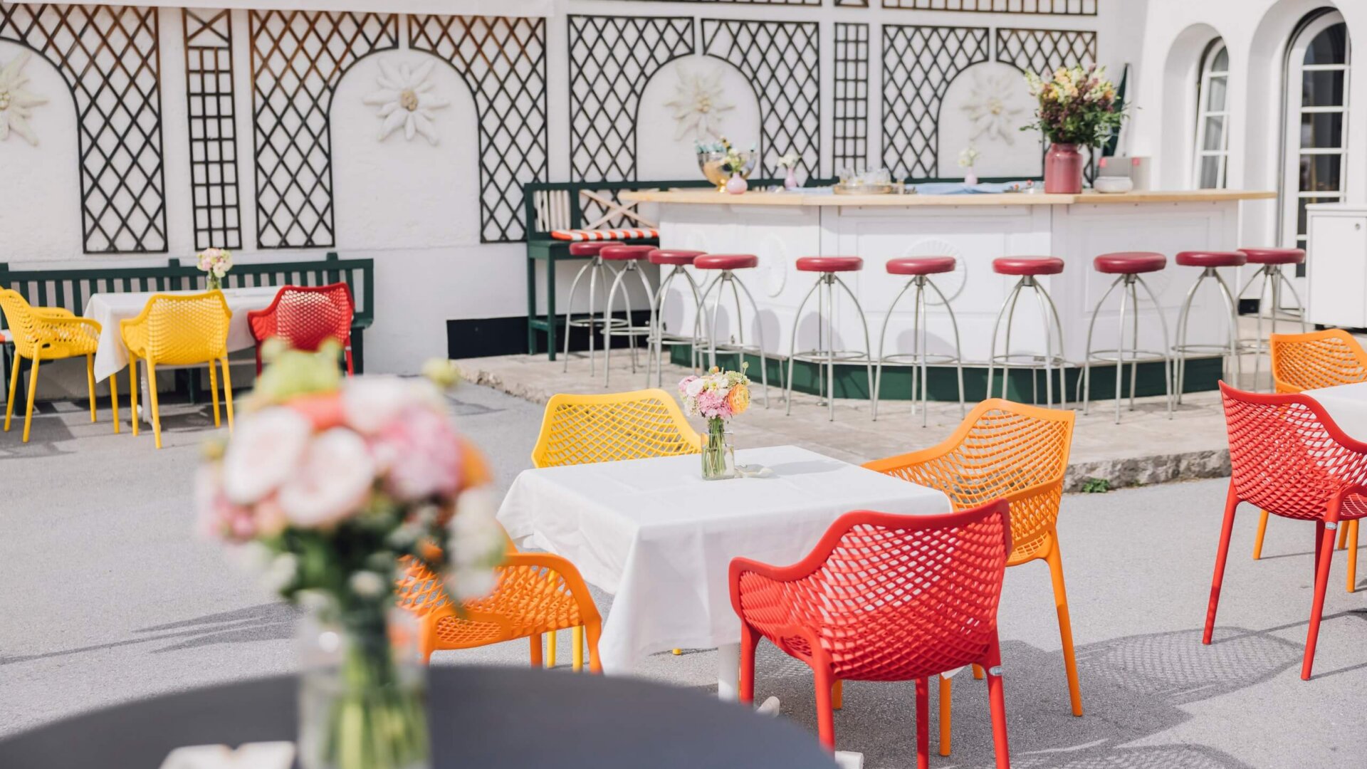 Bunte Sitzmöbel auf der Terrasse des Hotel Edelweiss in Lech/Zürs, umgeben von frischen Blumen und einer einladenden Bar.