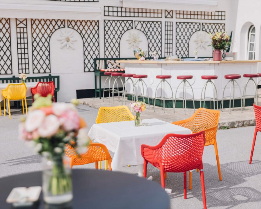 Bunte Sitzmöbel auf der Terrasse des Hotel Edelweiss in Lech/Zürs, umgeben von frischen Blumen und einer einladenden Bar.