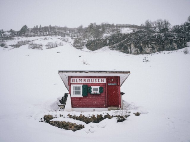 Rote Hütte im Schnee mit dem Schriftzug Almrausch in einer winterlichen Landschaft in Lech/Zürs am Arlberg.