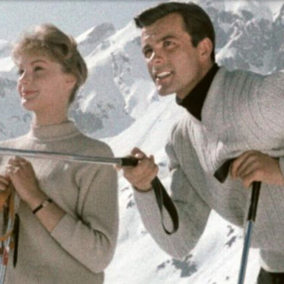 Paar beim Skifahren in den Bergen, lächelnd vor einer schneebedeckten Bergkulisse in Lech/Zürs am Arlberg.