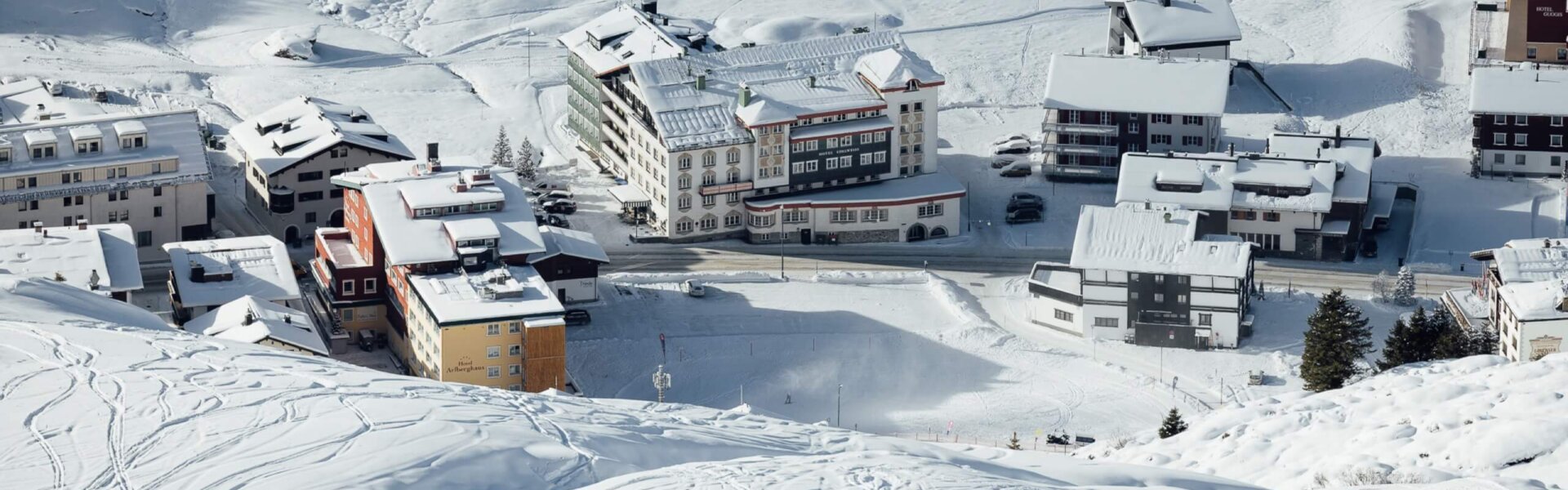 Winterliche Aussicht auf das Hotel Edelweiss in Lech/Zürs mit verschneiten Bergen und Skipisten im Hintergrund.