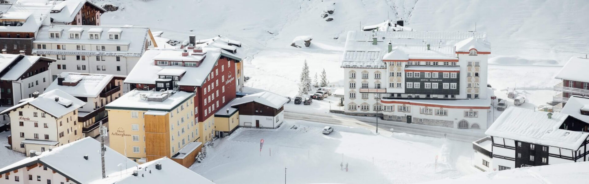 Winterliche Aussicht auf das Hotel Edelweiss in Lech/Zürs, umgeben von schneebedeckten Bergen und traditioneller Architektur.