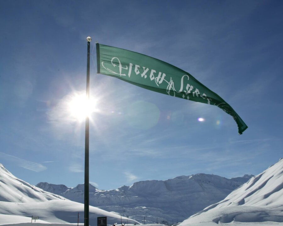 Flagge des Hotel Edelweiss weht im Schnee, vor einer beeindruckenden Berglandschaft in Lech/Zürs am Arlberg.