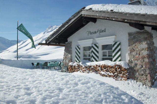 Historisches Hüttenambiente im winterlichen Lech mit Blick auf schneebedeckte Berge und gemütlicher Terrasse.