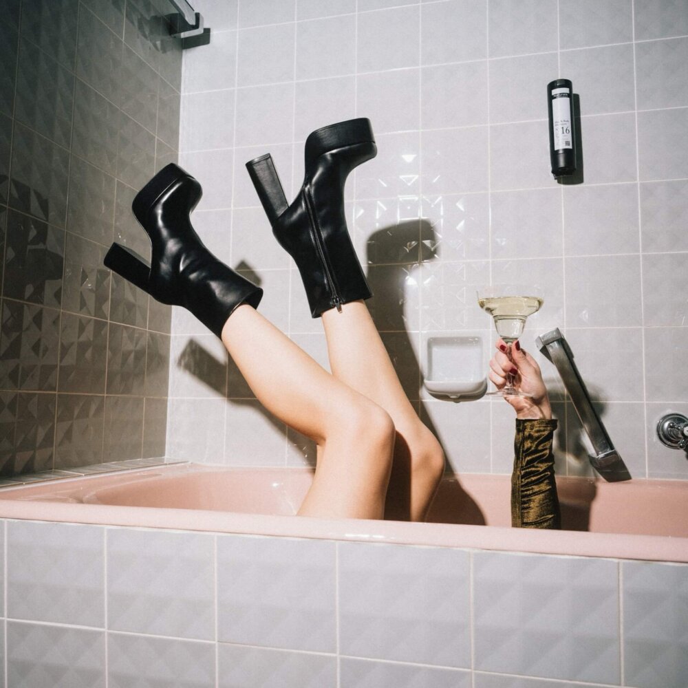 Füße in hohen Schuhen zeigen Genussmoment in Badewanne mit Cocktail, stilvoller Bezug zu Hotel Edelweiss in Lech.