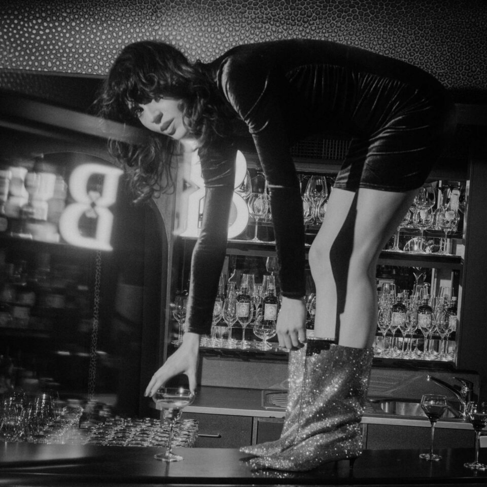 Elegante Frau in funkelnden Stiefeln, die Drinks an der Bar im Hotel Edelweiss in Lech/Zürs serviert.