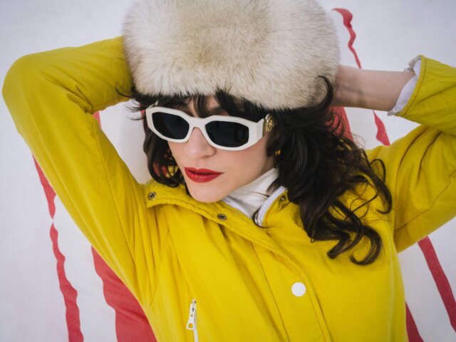 Frau in gelber Jacke und weißen Sonnenbrillen mit Pelzmütze, entspannt im Schnee im Hotel Edelweiss, Lech/Zürs.