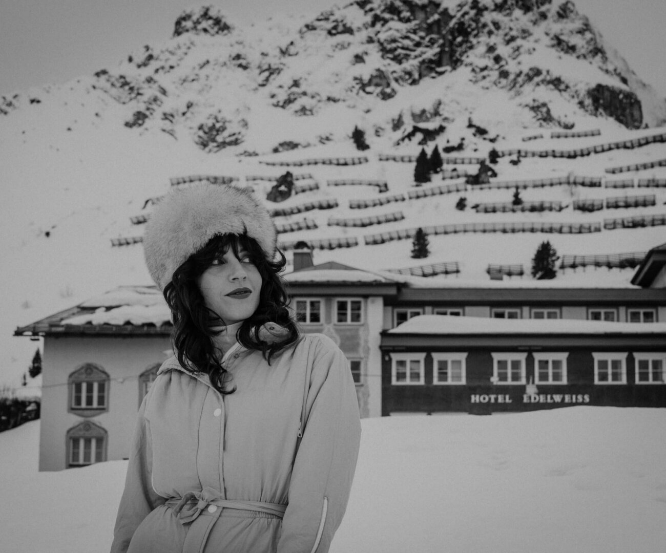 Frau mit Pelzmütze vor dem Hotel Edelweiss in der verschneiten Winterlandschaft von Lech/Zürs am Arlberg.