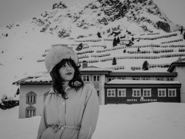 Frau mit Pelzmütze vor dem Hotel Edelweiss in der verschneiten Winterlandschaft von Lech/Zürs am Arlberg.