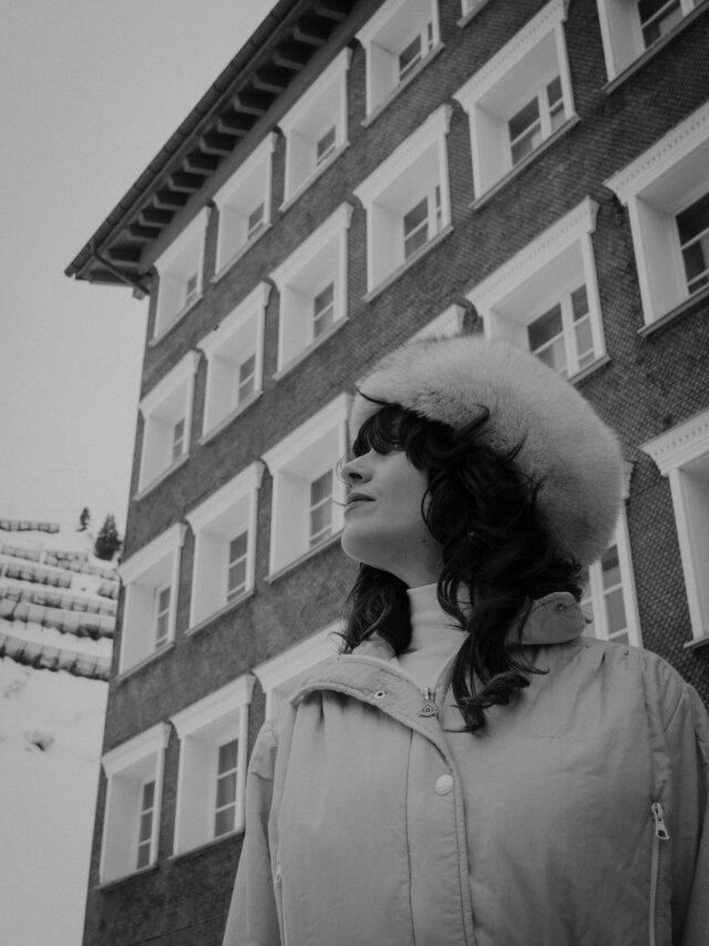 Frau im Winterlook steht vor dem Hotel Edelweiss in Lech/Zürs, umgeben von einer malerischen Berglandschaft.