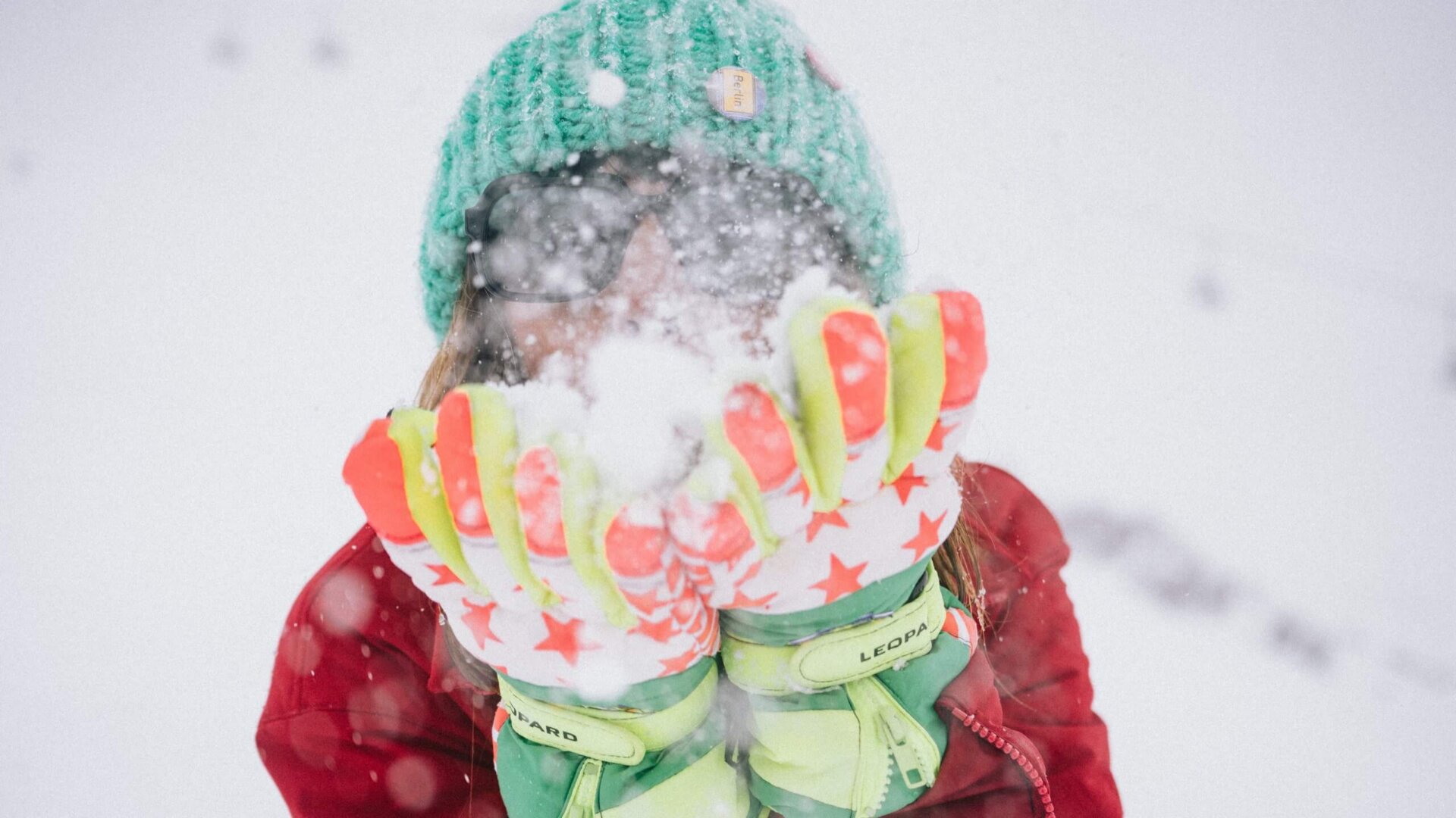 Frau im Schnee, die mit bunten Handschuhen Schnee wirbelt, ideal für die Wintersaison im Hotel Edelweiss, Lech/Zürs.