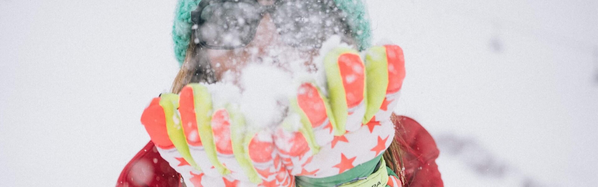 Frau im Schnee, die mit bunten Handschuhen Schnee wirbelt, ideal für die Wintersaison im Hotel Edelweiss, Lech/Zürs.