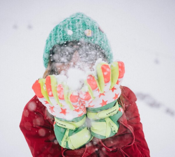 Frau im Schnee, die mit bunten Handschuhen Schnee wirbelt, ideal für die Wintersaison im Hotel Edelweiss, Lech/Zürs.
