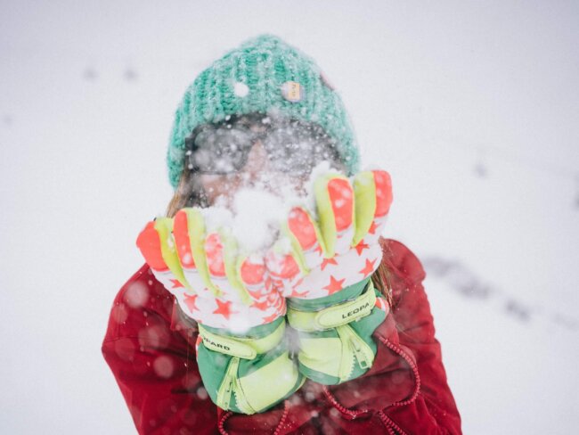 Frau im Schnee, die mit bunten Handschuhen Schnee wirbelt, ideal für die Wintersaison im Hotel Edelweiss, Lech/Zürs.