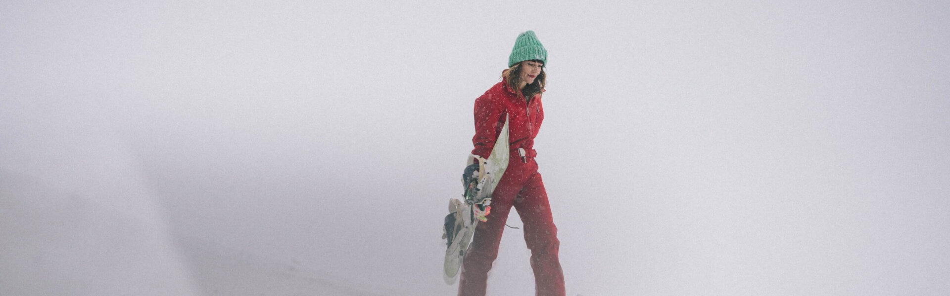 Eine Frau in roter Skibekleidung wandert durch verschneite Landschaft im Nebel, ideal für Winterabenteuer in Lech/Zürs.