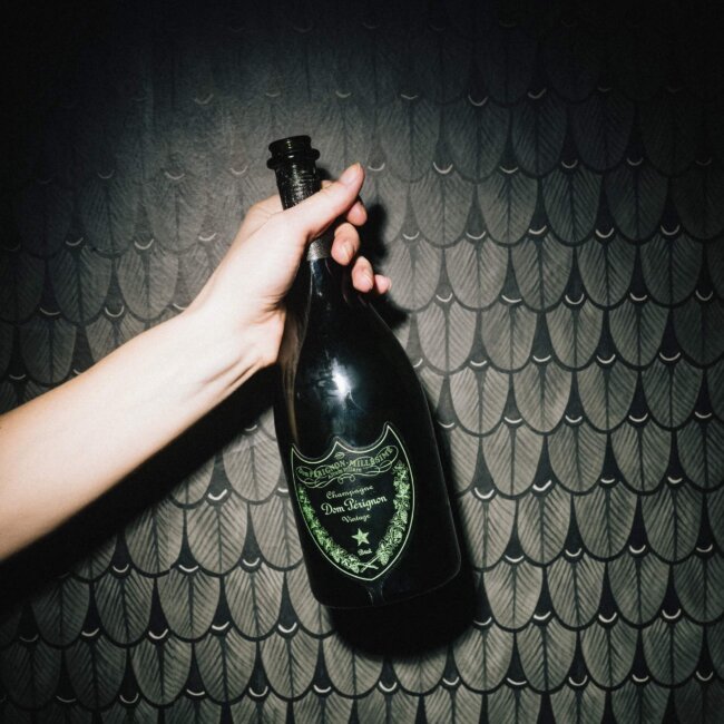 Hand hält eine Flasche Dom Pérignon Champagner vor einer elegant gestalteten Wand im Hotel Edelweiss in Lech/Zürs.