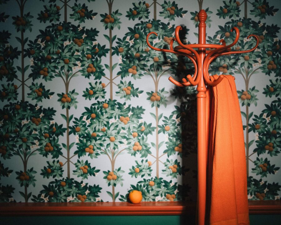 Bunter Garderobenständer mit orangefarbener Jacke vor einer grünen Blumenwand im Hotel Edelweiss, Lech/Zürs.