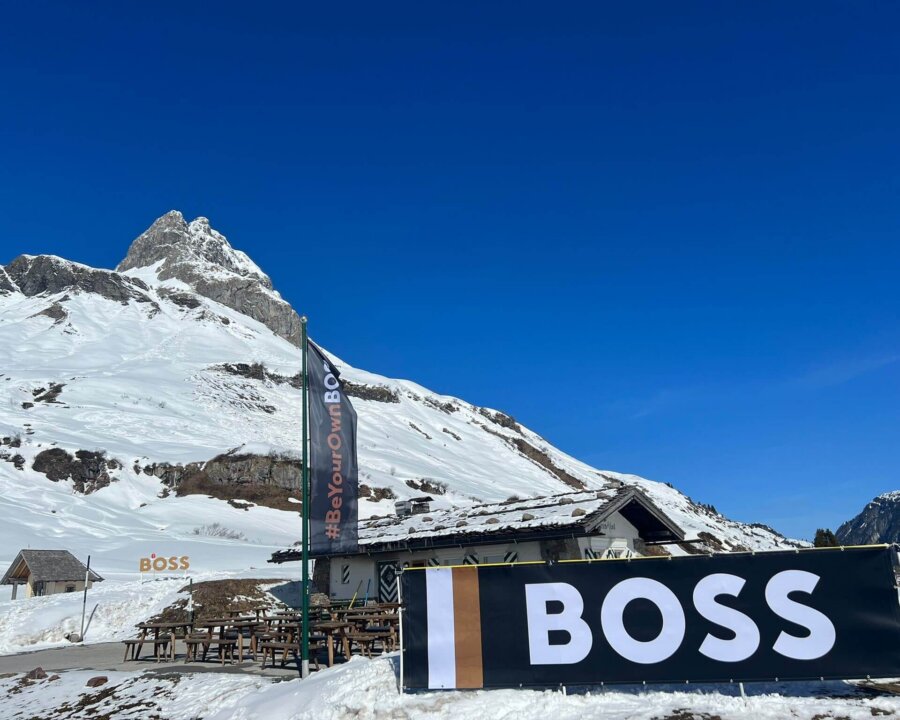 Schneebedeckte Berge mit einem Restaurant und einem großen Werbebanner in Lech/Zürs am Arlberg bei klarem blauen Himmel.