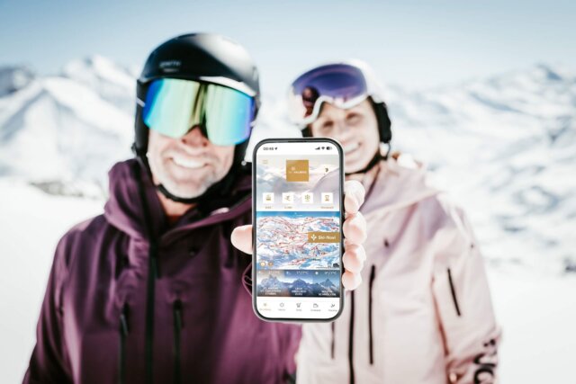 Skifahrer zeigen stolz die Ski-App vor atemberaubender Berglandschaft in Lech/Zürs am Arlberg.