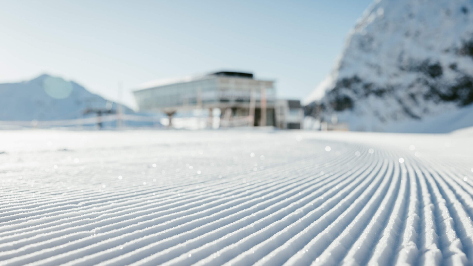 Schneebedeckter Hang mit kunstvollen Spuren und dem Hotel Edelweiss im Hintergrund, umgeben von beeindruckenden Bergen.