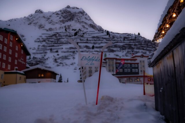 Eislaufplatz in Zürs mit Blick auf das Hotel Edelweiss und die verschneiten Berge im Hintergrund. Winterliche Atmosphäre.