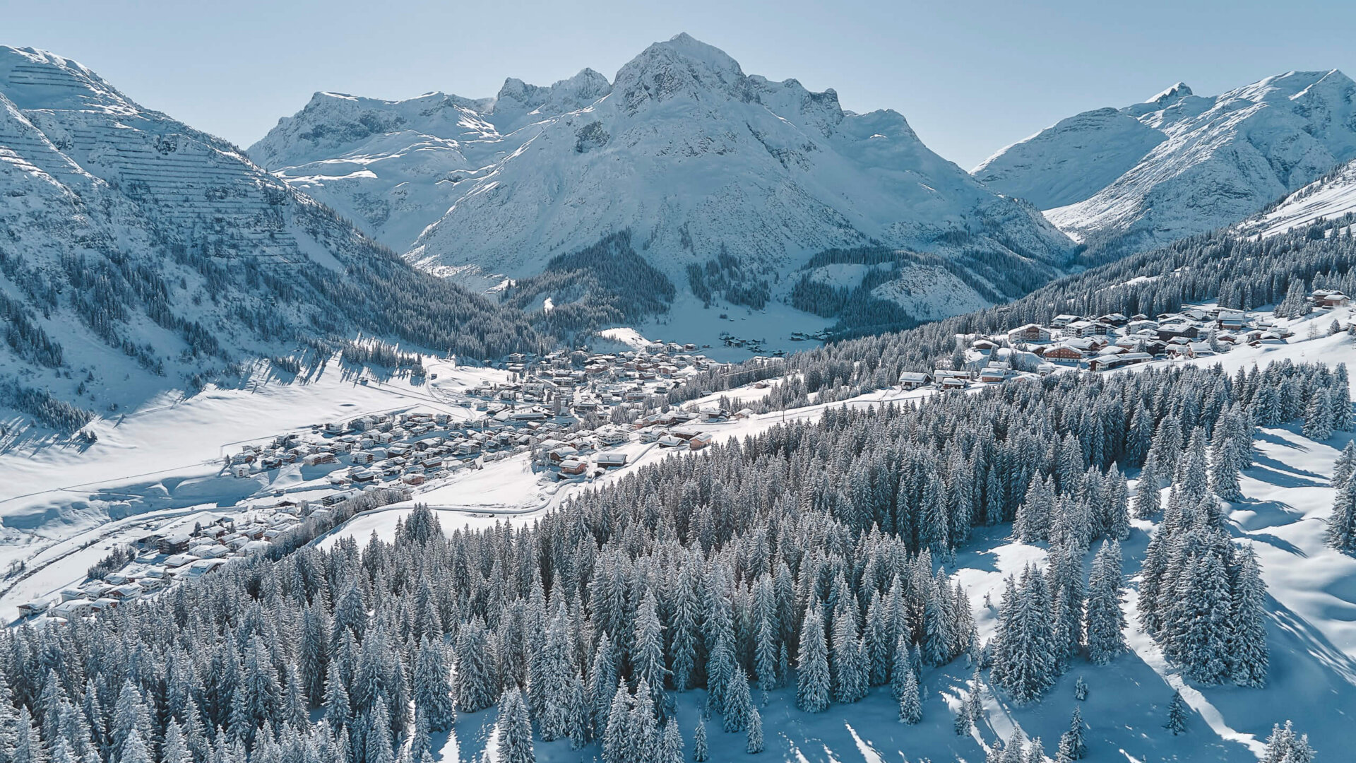 Winterliche Landschaft über Lech/Zürs am Arlberg mit schneebedeckten Bergen und einem charmanten Dorf in der Ferne.